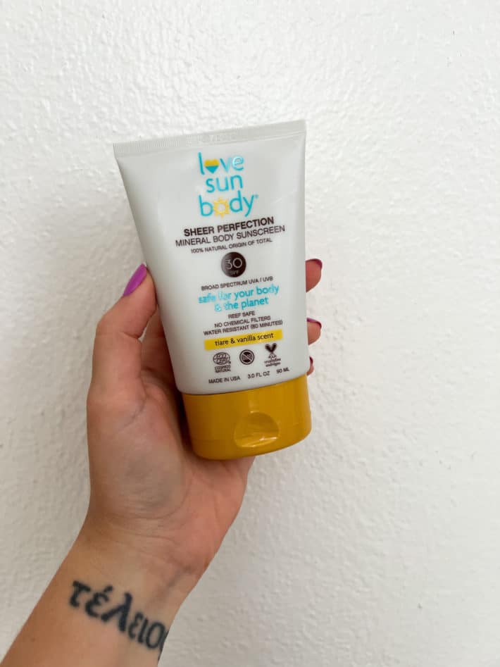 a hand holds up Love Sun Body SPF 30 Tiare and Vanilla Scent.