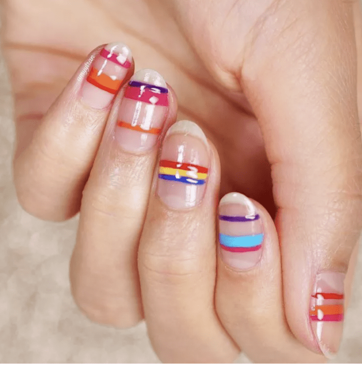 a close up of a hand with multi colored stripes of nail polish