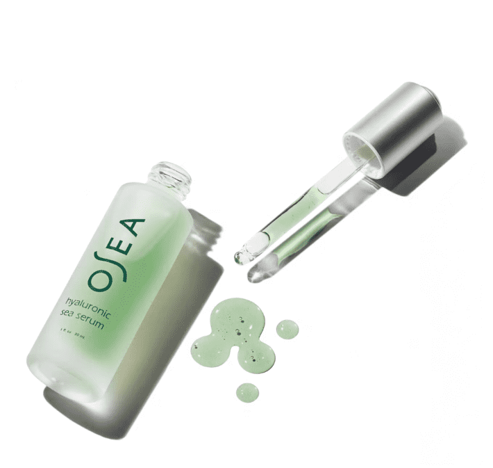 an open bottle of OSEA Hyaluronic Sea Serum lays down with the dropper top beside it and it's green contents nearby