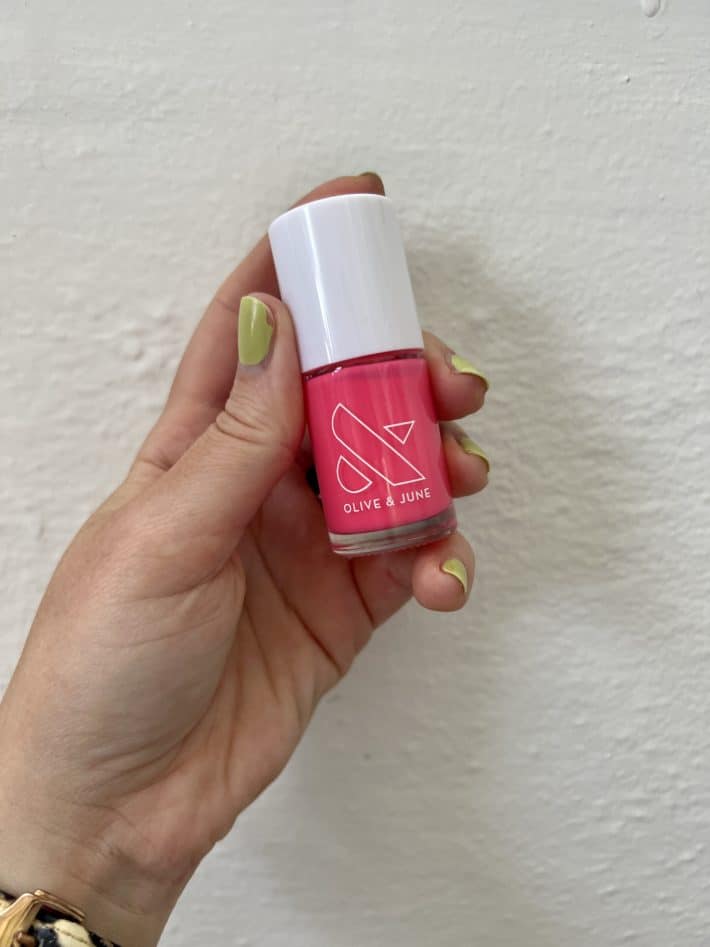 a hand holds a bottle of olive and june hot strawberry nail polish