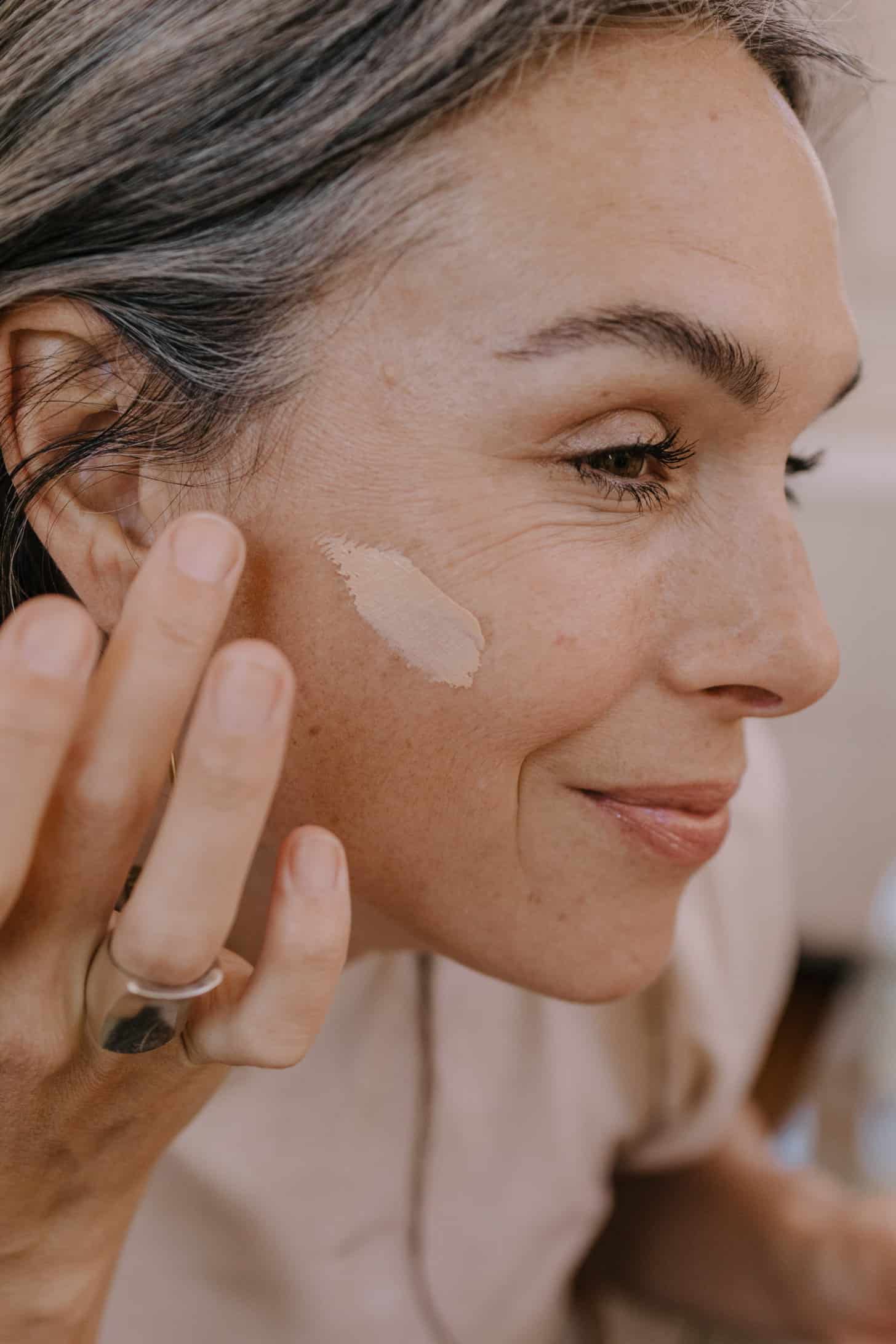 a woman wipes non-toxic tinted face spf on her cheek while smiling