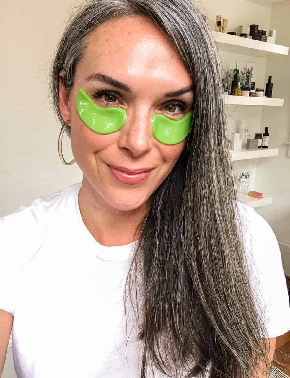 a woman wears green eye gels while smiling at the camera