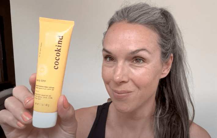 A woman holds up a tube of cocokind spf
