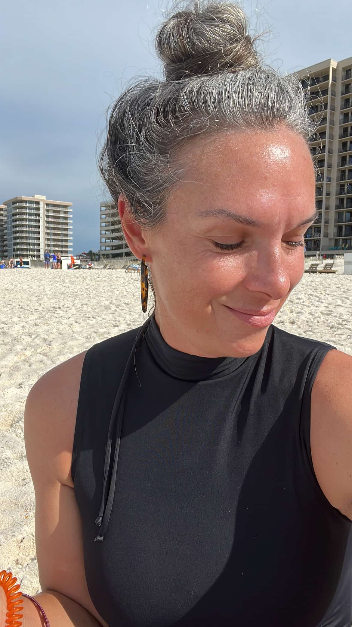 a woman with her hair in bun looks down while standing on the beach