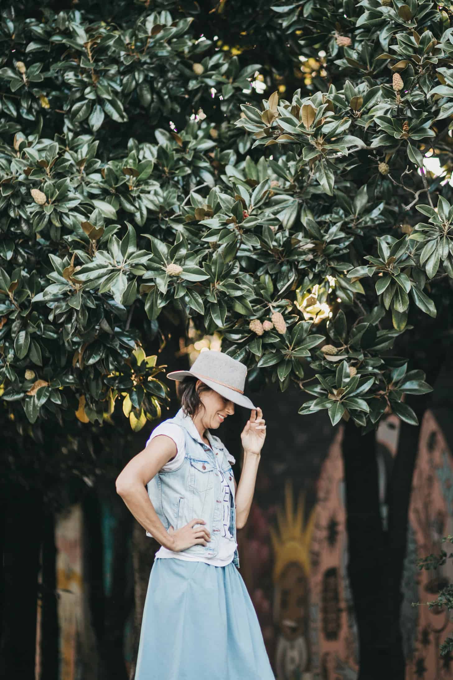 a woman wearing a hat stands amidst some trees