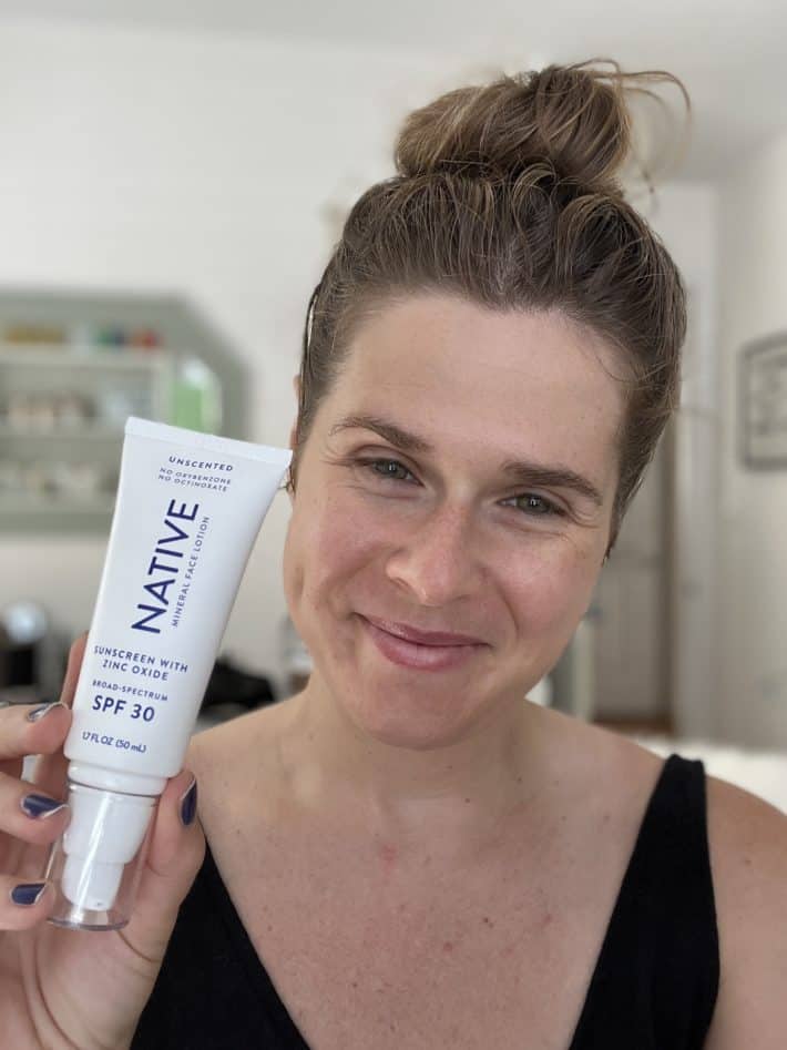 a woman holding up a tube of native face spf 30