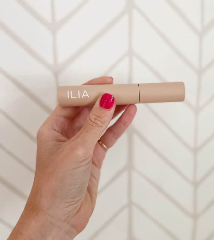 a hand holds up a tube of ILIA fullest volumizing mascara