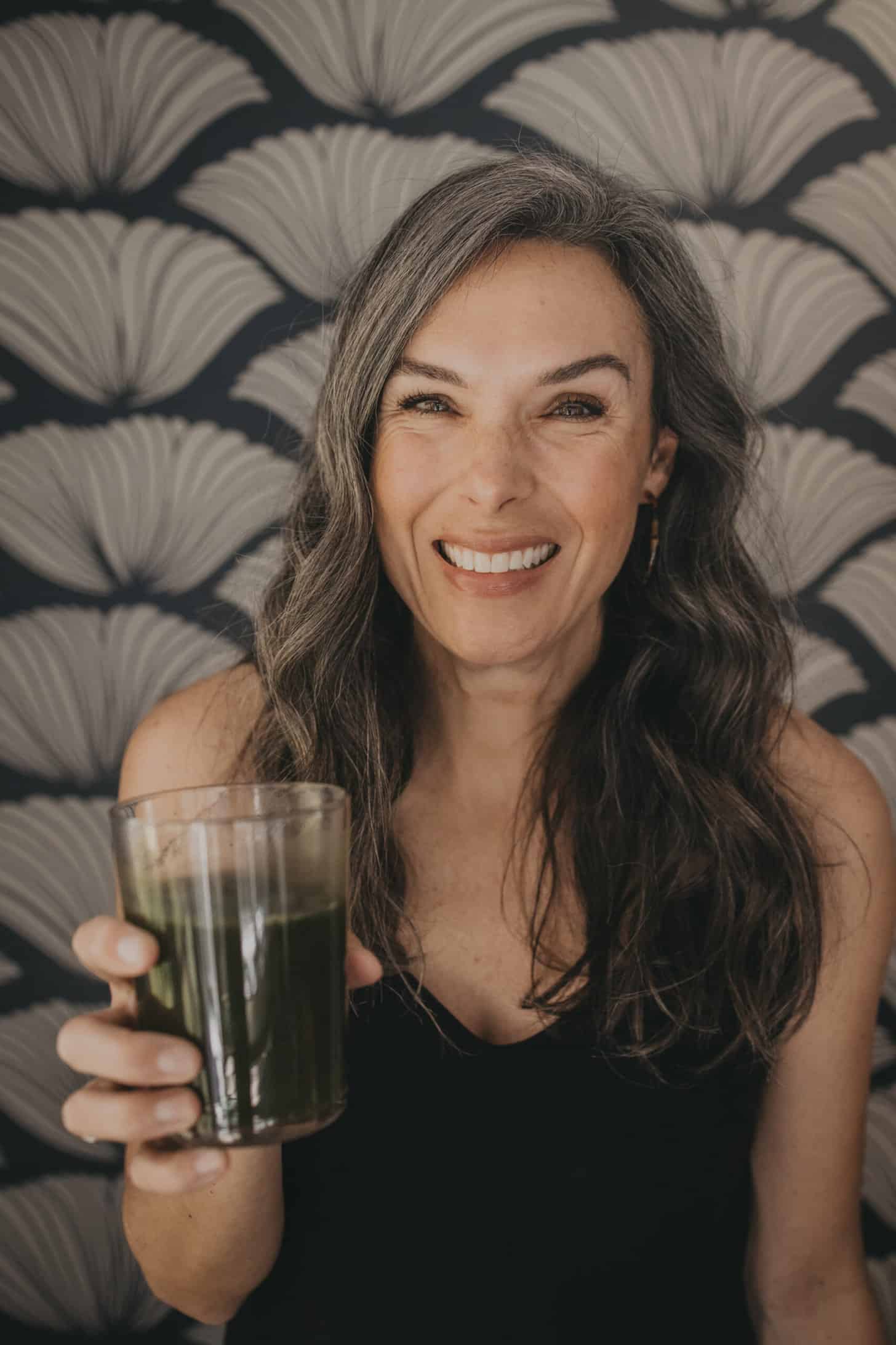 a woman holds up a glass of green juice