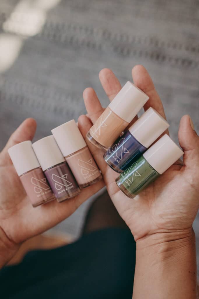 a hand holds six different nail polish bottles by olive and june