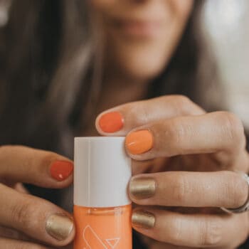 a woman holds up a bottle of orange nail polish from olive and june