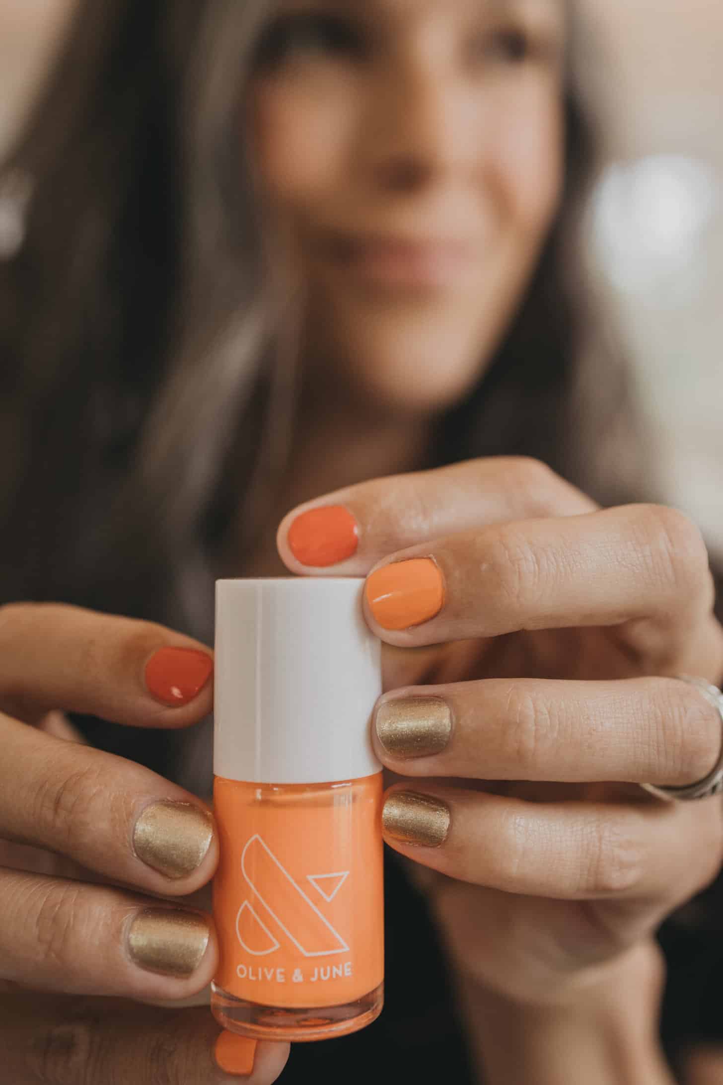 a woman holds up a bottle of orange nail polish from olive and june