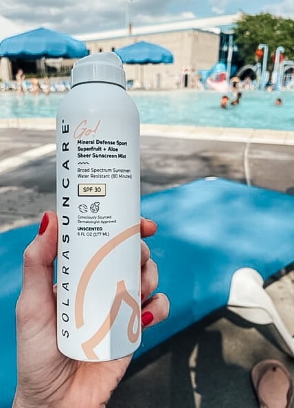 a bottle of solara suncare go spray sunscreen is held up with a pool in the background