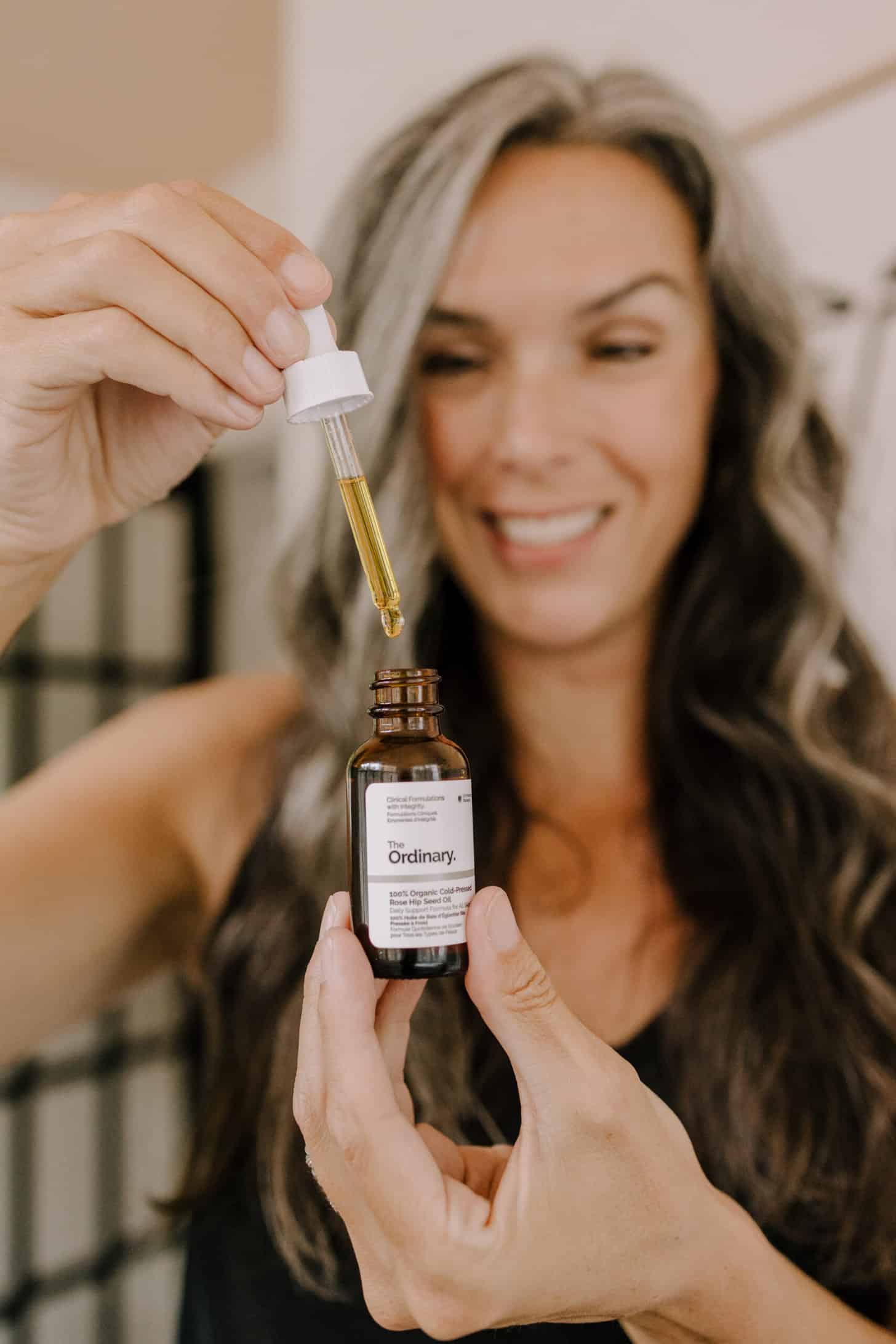 a woman holds up a bottle and dropper of The Ordinary organic cold pressed rose hip seed oil
