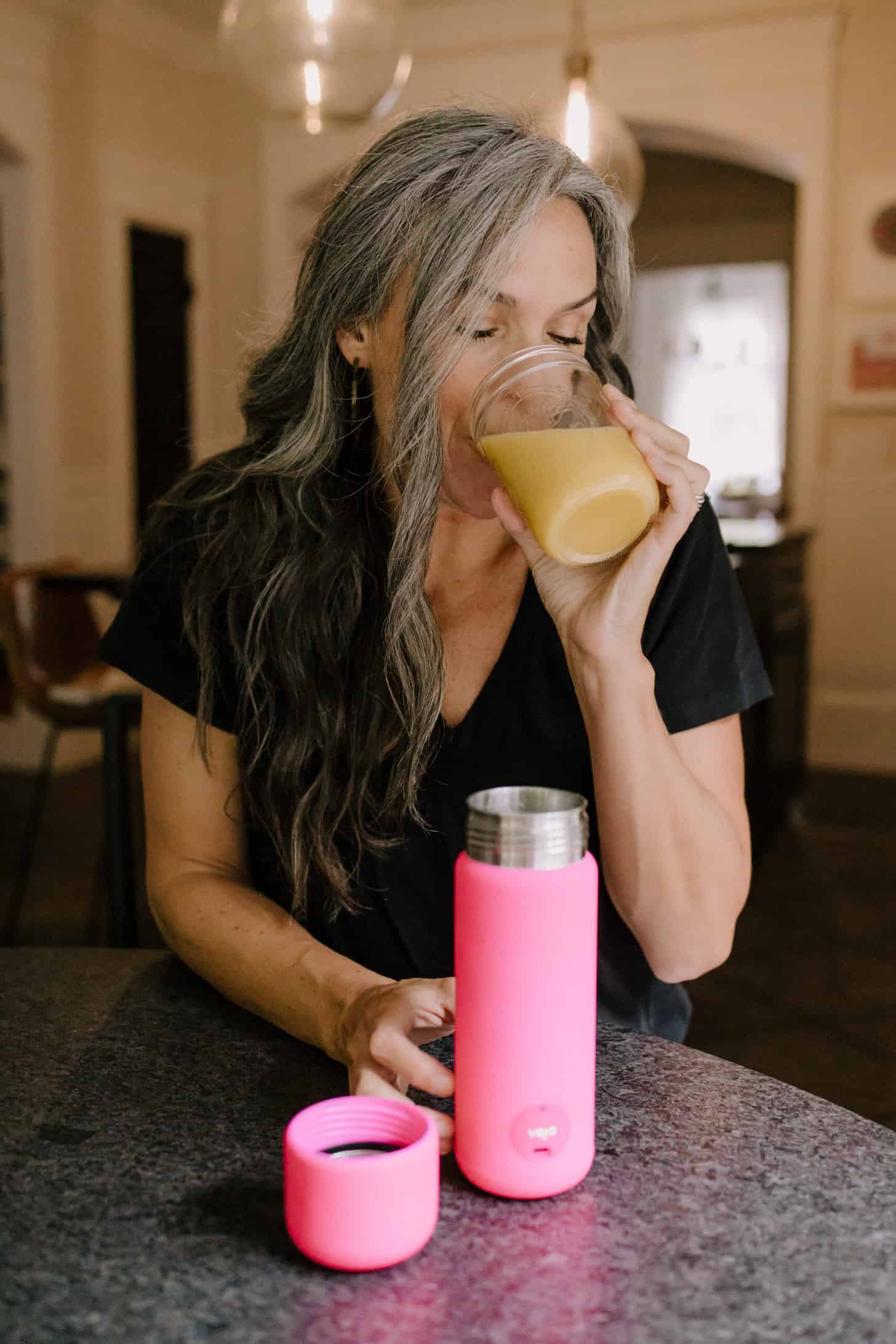 a hot pink portable blender sit on a table in front of a woman drinking a blended drink