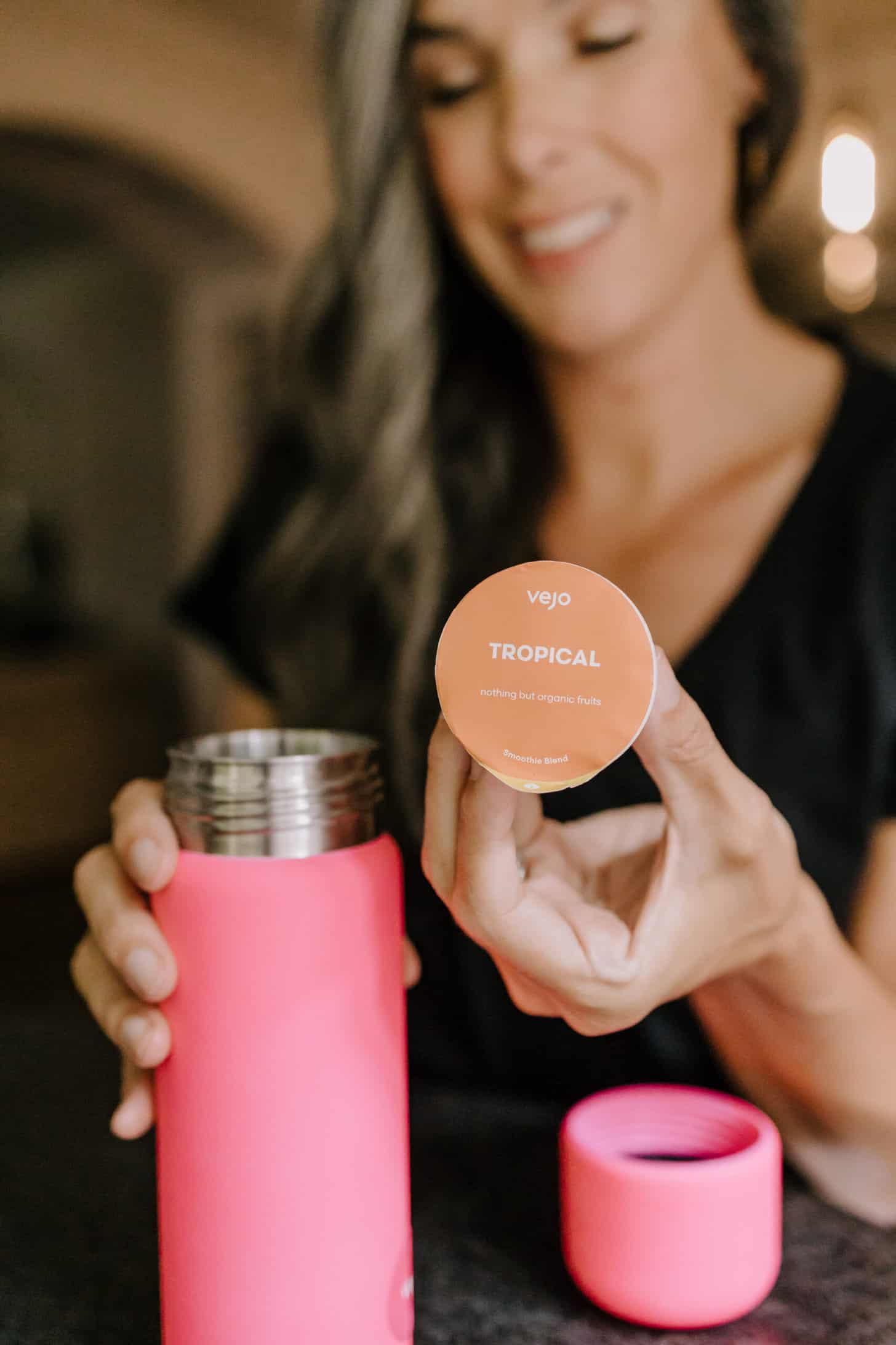 in the foreground a hot pink portable blender and blend capsule are held by a woman in the background