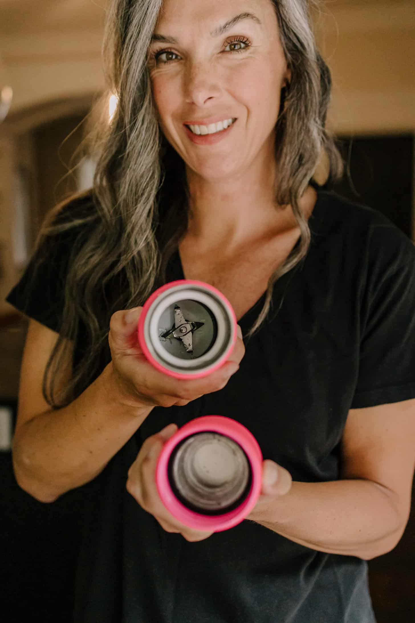 a woman with long gray hair holds up a hot pink portable blender so that the inside of it is visible
