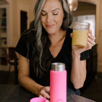 a woman smiles as she looks down at a hot pink portable blender