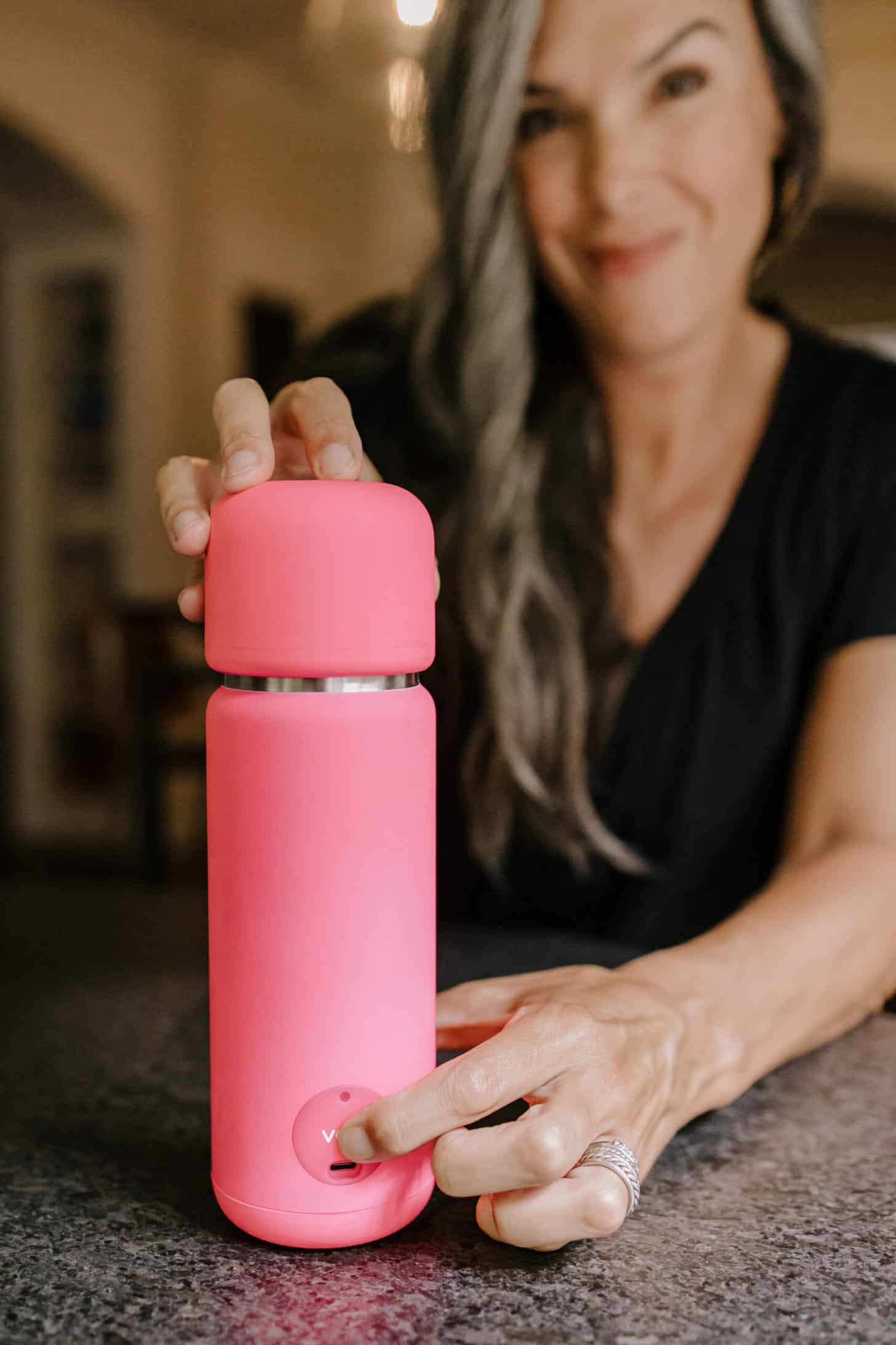a close up of a hot pink portable blender with a woman in a black shirt in the background