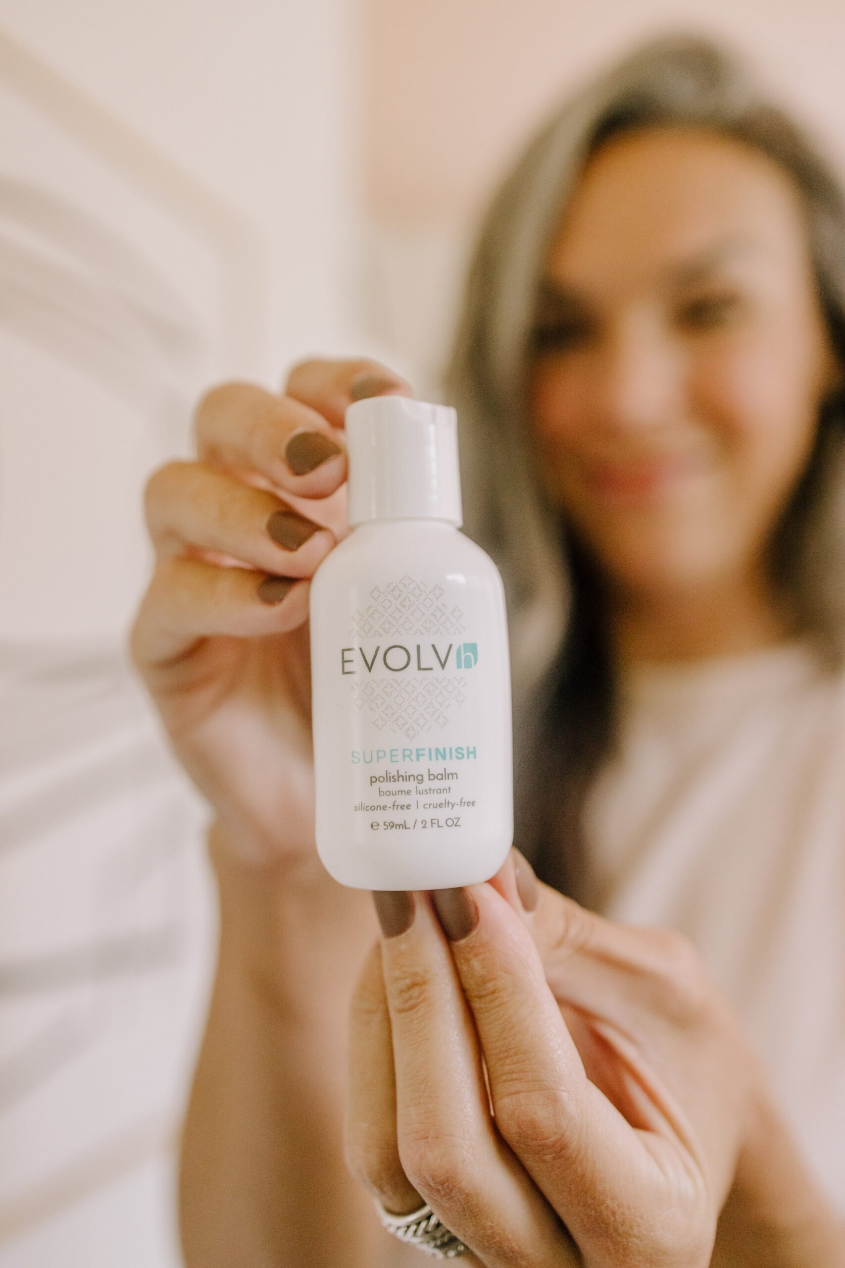 a woman holds up a travel sized bottle of evolvh's super finish polishing balm