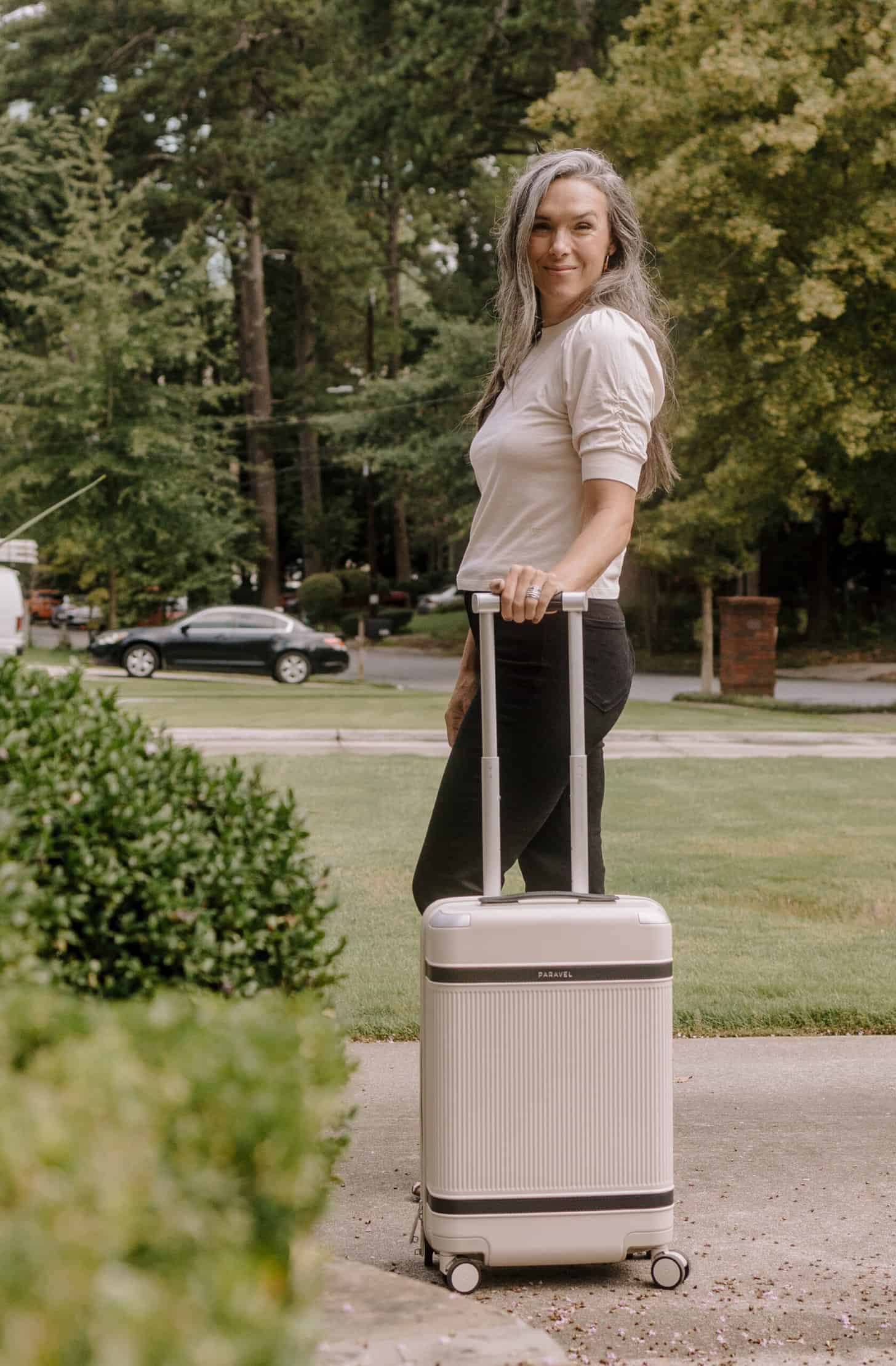 a woman stands outside with her carry on plus bag
