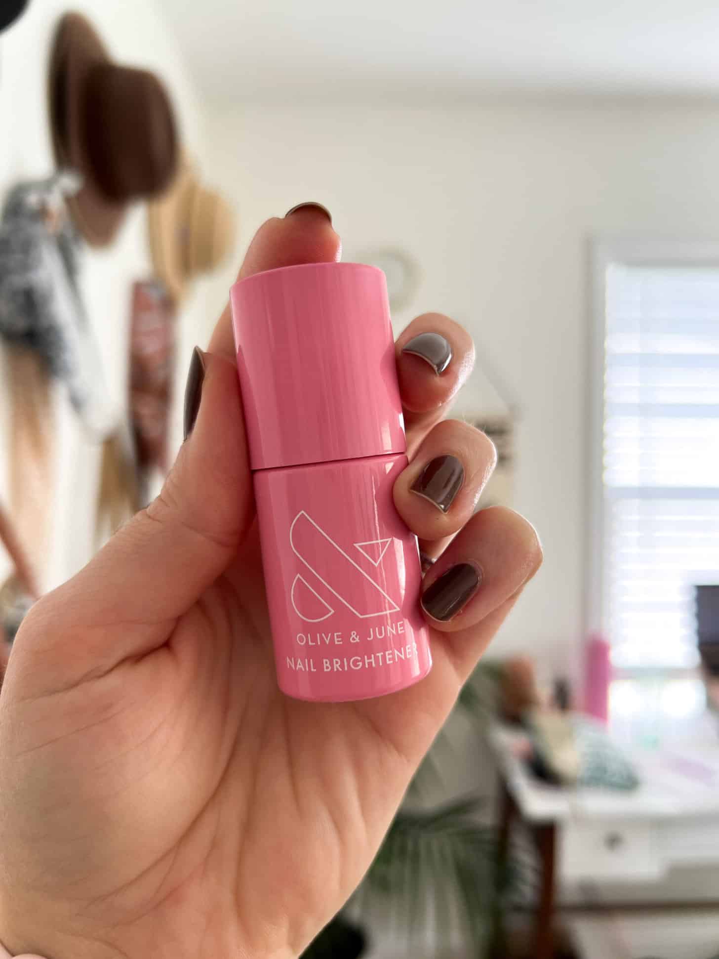 A hand holds up a bottle of Olive & June Nail Brightener.