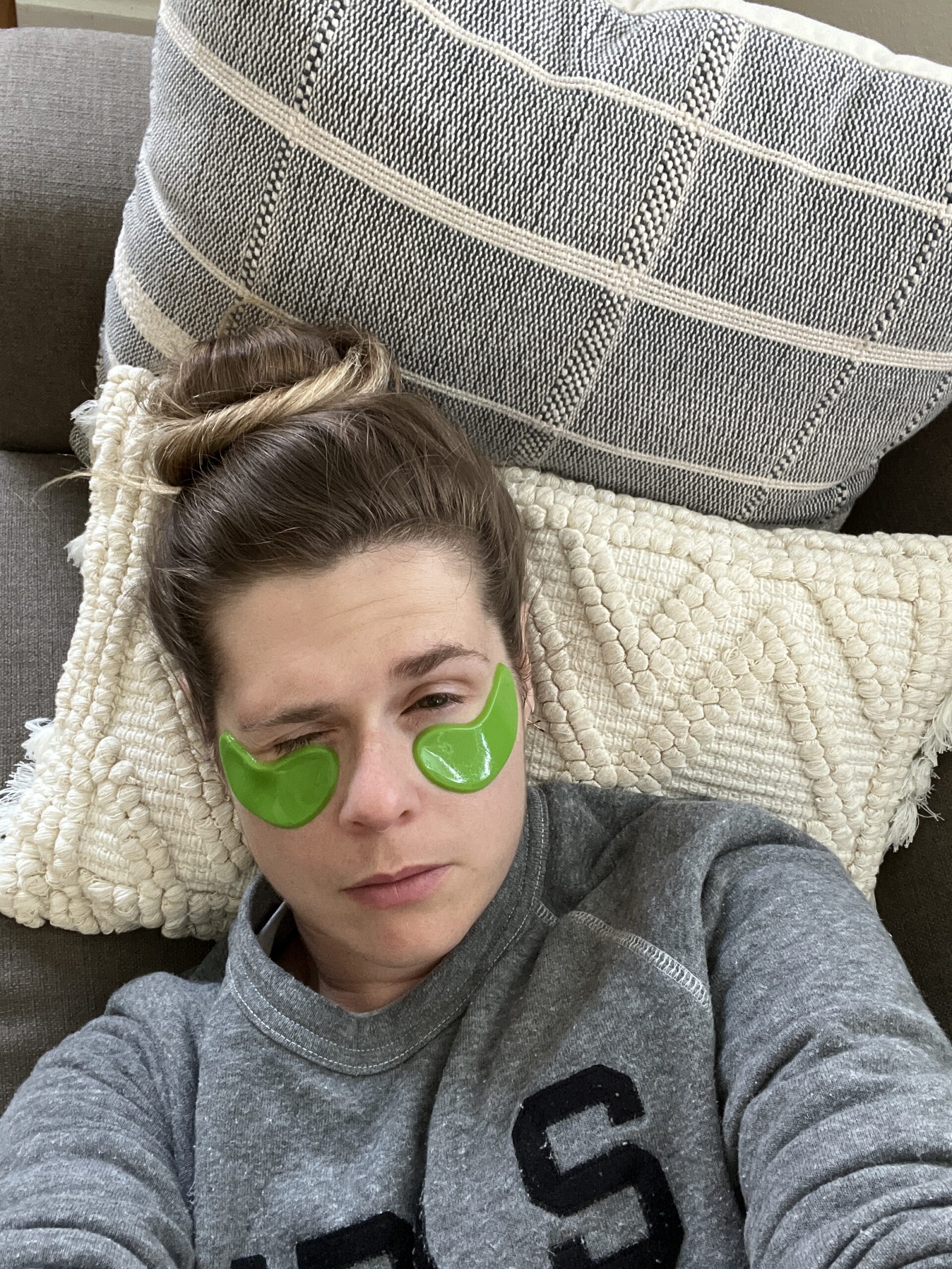 A woman lays on her sofa with green 100% pure eye gels under her eyes.