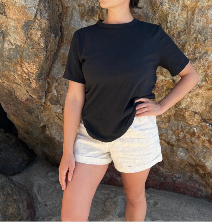 A woman in a black t-shirt and shorts stands in front of a rock.