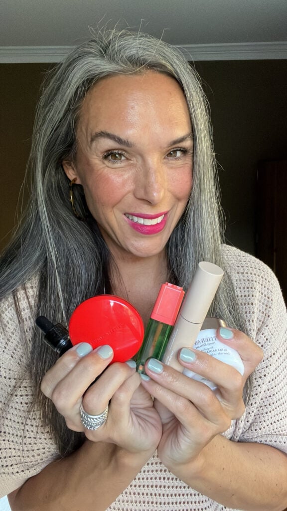 A woman smiles and holds makeup from Credo Beauty