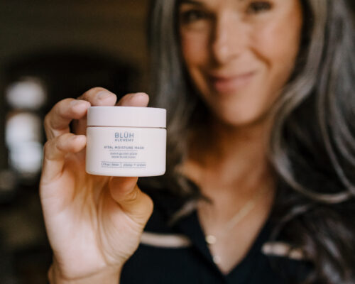 A woman holds up a moisture mask from BLUH Alchemy