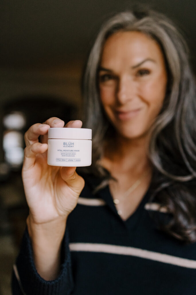 A woman holds up a moisture mask from BLUH Alchemy