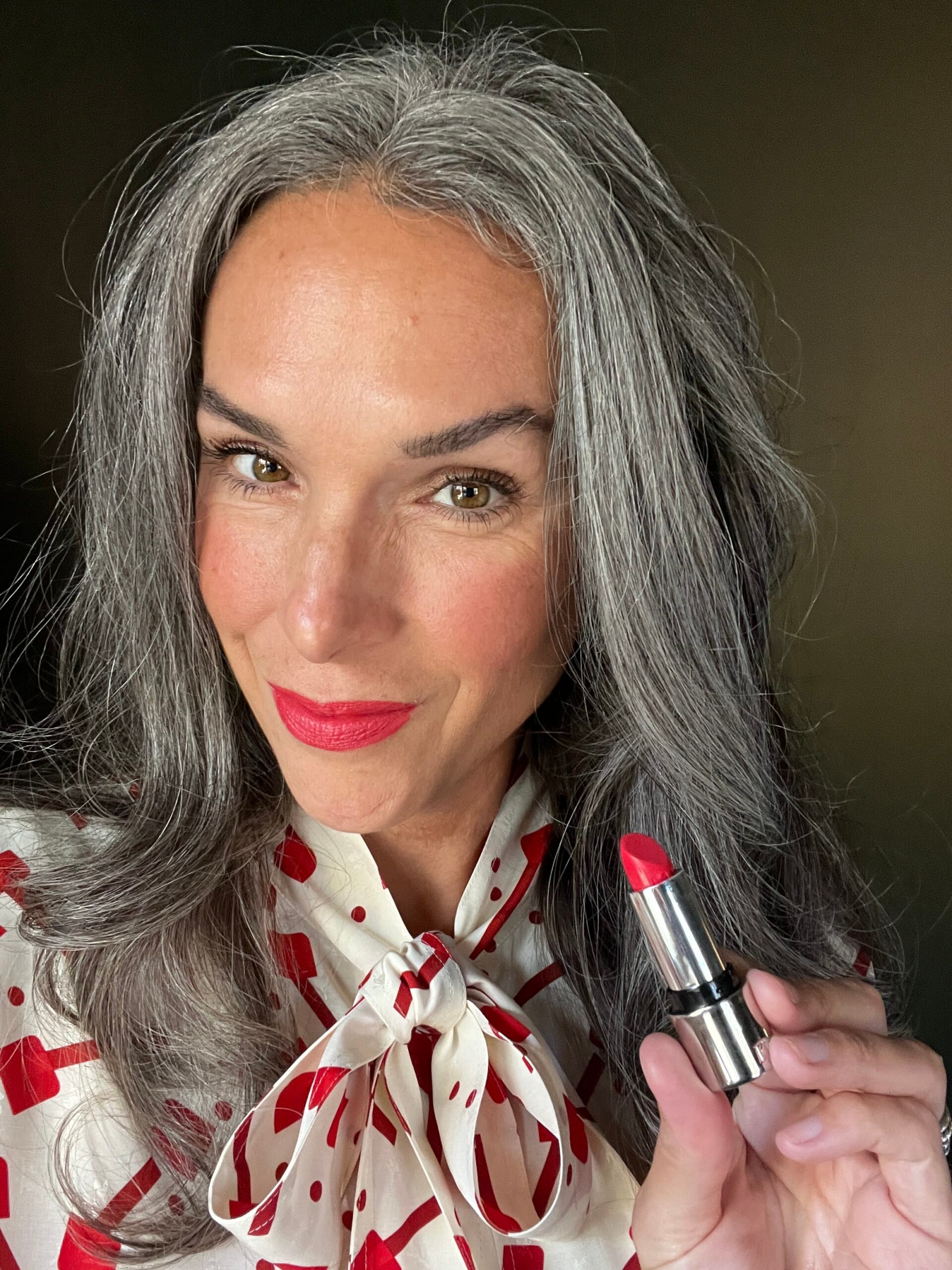 kjaer weis red lipstick applied to woman with gray hair wearing a white and red shirt