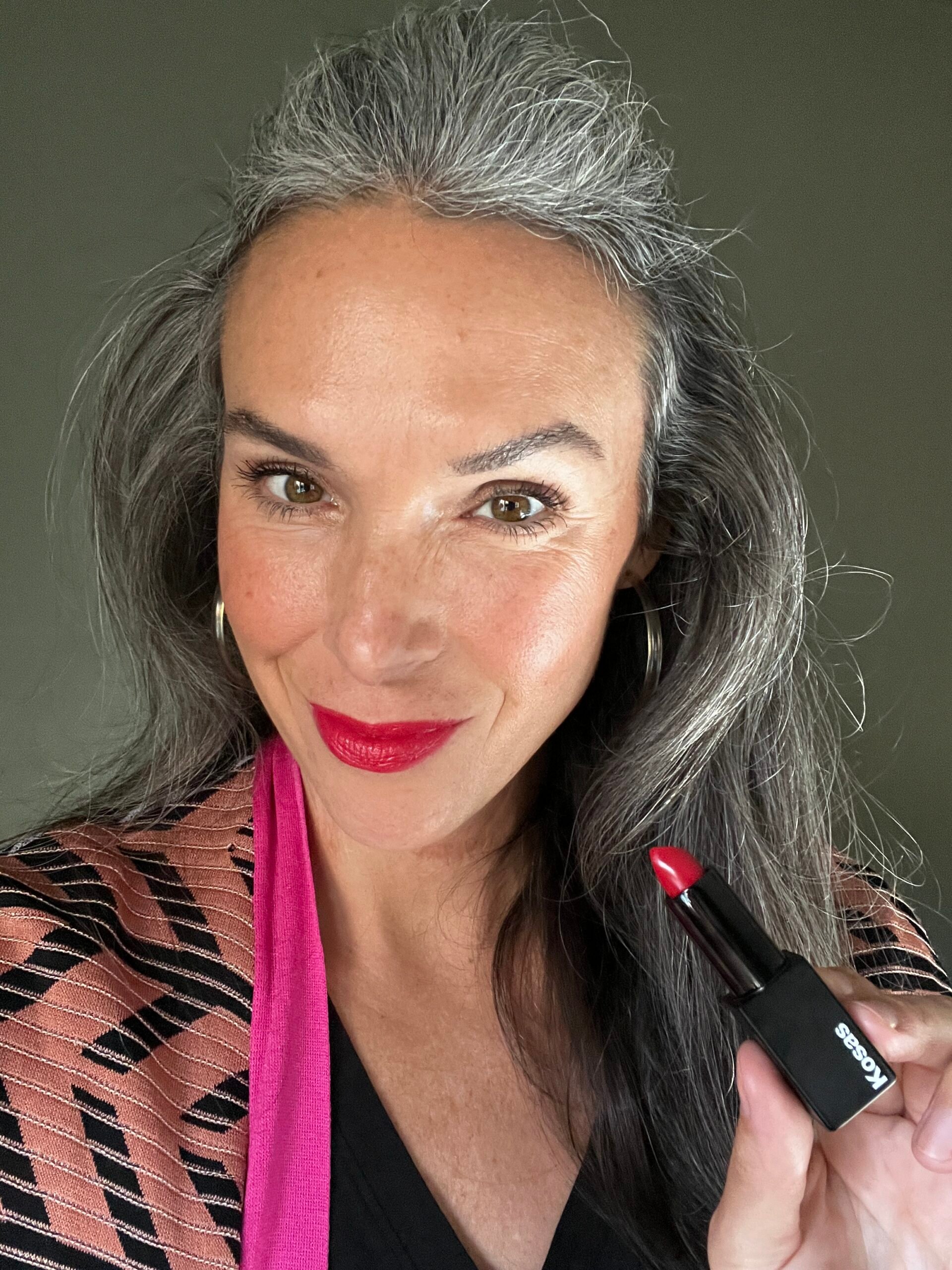 Kosas Weightless Lipstick in Electra on a woman's lips as she holds up the tube of it. 