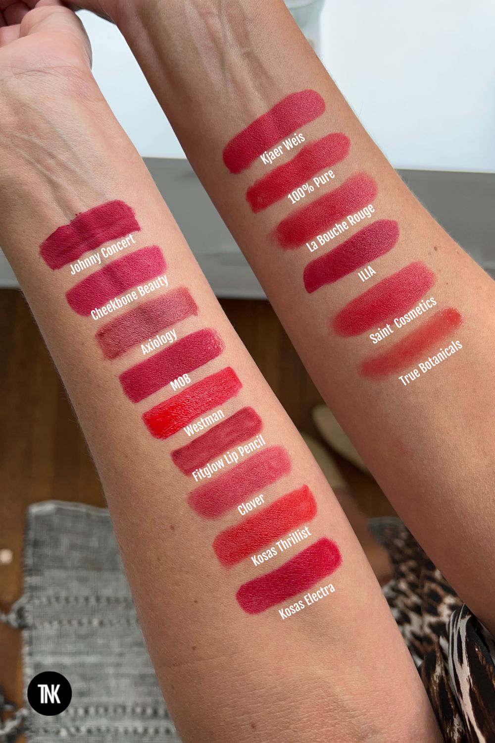 Swatches of red lipsticks on a woman's arm with labels of their brand name.