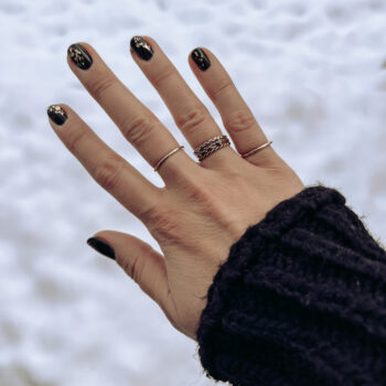 A hand with black painted nails is held in front of a snowy background.