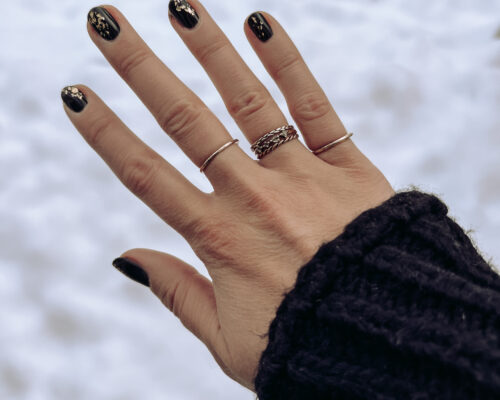 A hand with black painted nails is held in front of a snowy background.