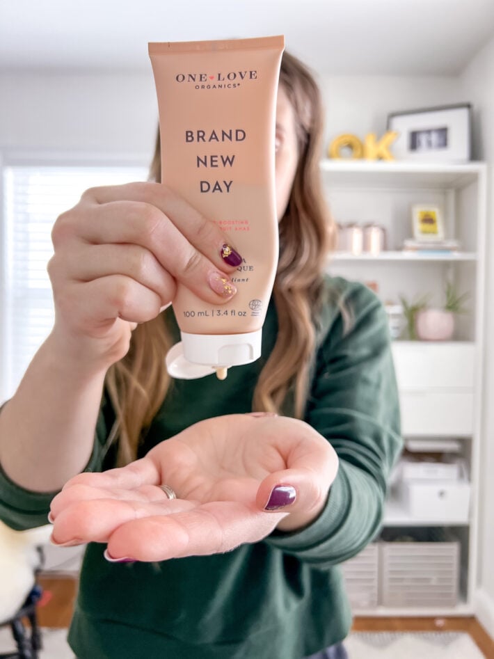 A woman squeezes a tube of One Love Organics Brand New Day into her hand.