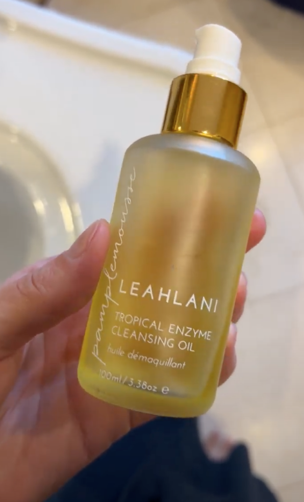 A hand holds up a bottle of leahlani cleanser.