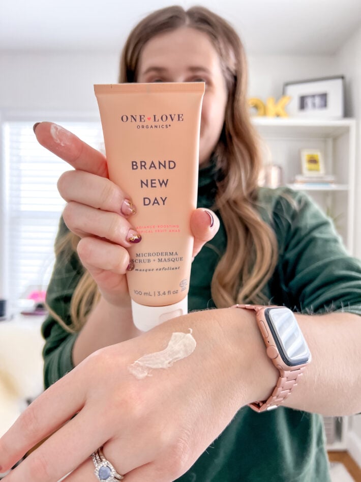 A woman holds up a tube of One Love Organics Brand New Day masque.
