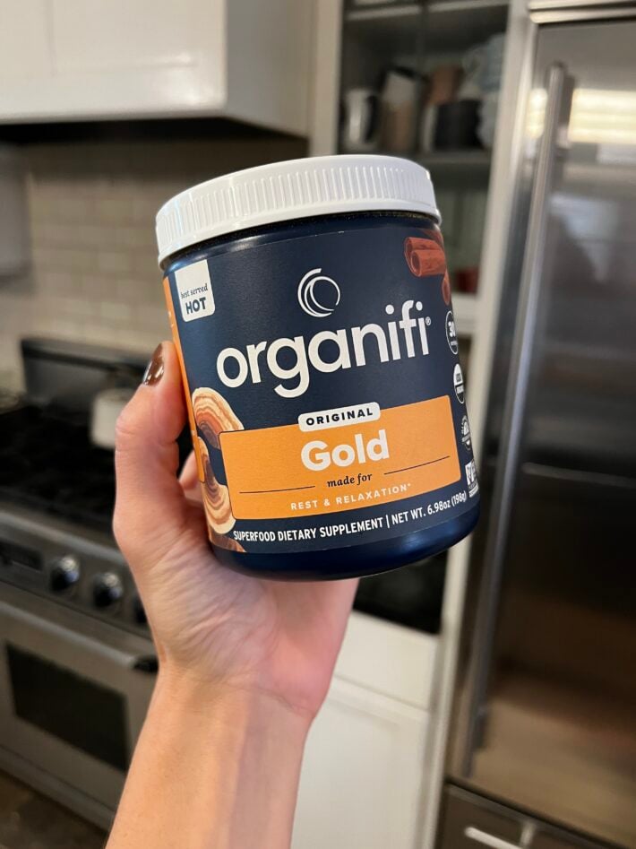 A hand holding up a canister of Organifi Gold