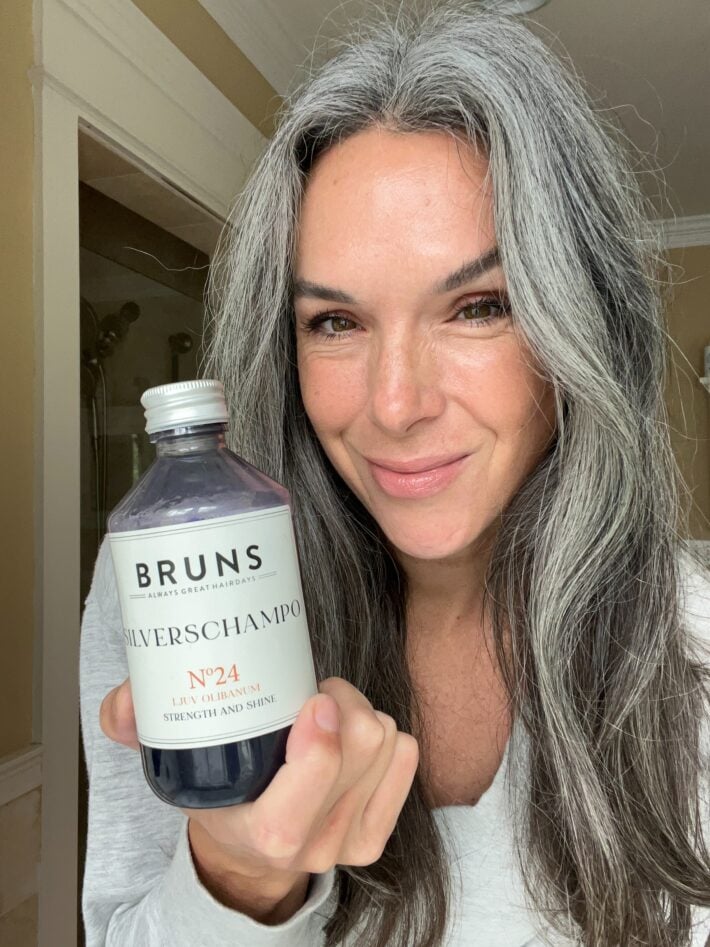 A bottle of Bruns SCHAMPO N24 is held by a woman with long gray hair.