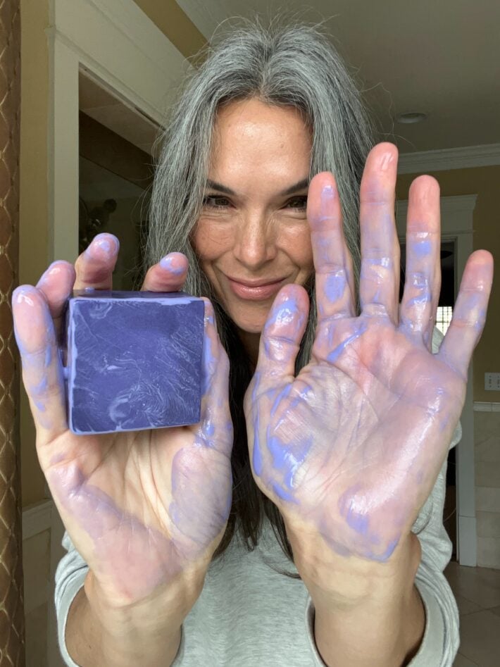 Ethique Tone It Down Brightening Purple Shampoo Bar once suds up on a woman's hands.
