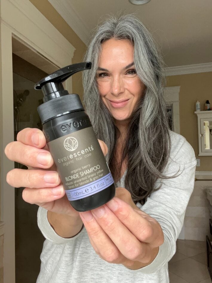 A bottle of EverEscents Organic Berry Blonde Shampoo is held in a woman's hand.