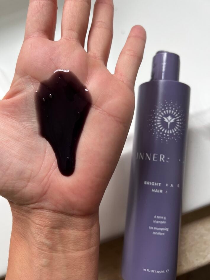 A bottle of Innersense Bright Balance Hairbath besides a hand with shampoo on the palm.