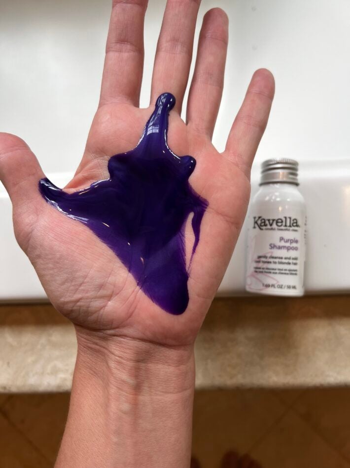 Kavella Purple Shampoo on a woman's hand plus a bottle of it sitting behind.