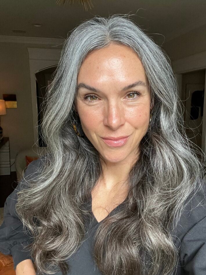 A woman with long wavy gray hair after using the Kitsch heatless curls set in her hair.