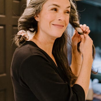 A woman with long wavy gray hair takes her hair out of the Kitsch heatless curls.