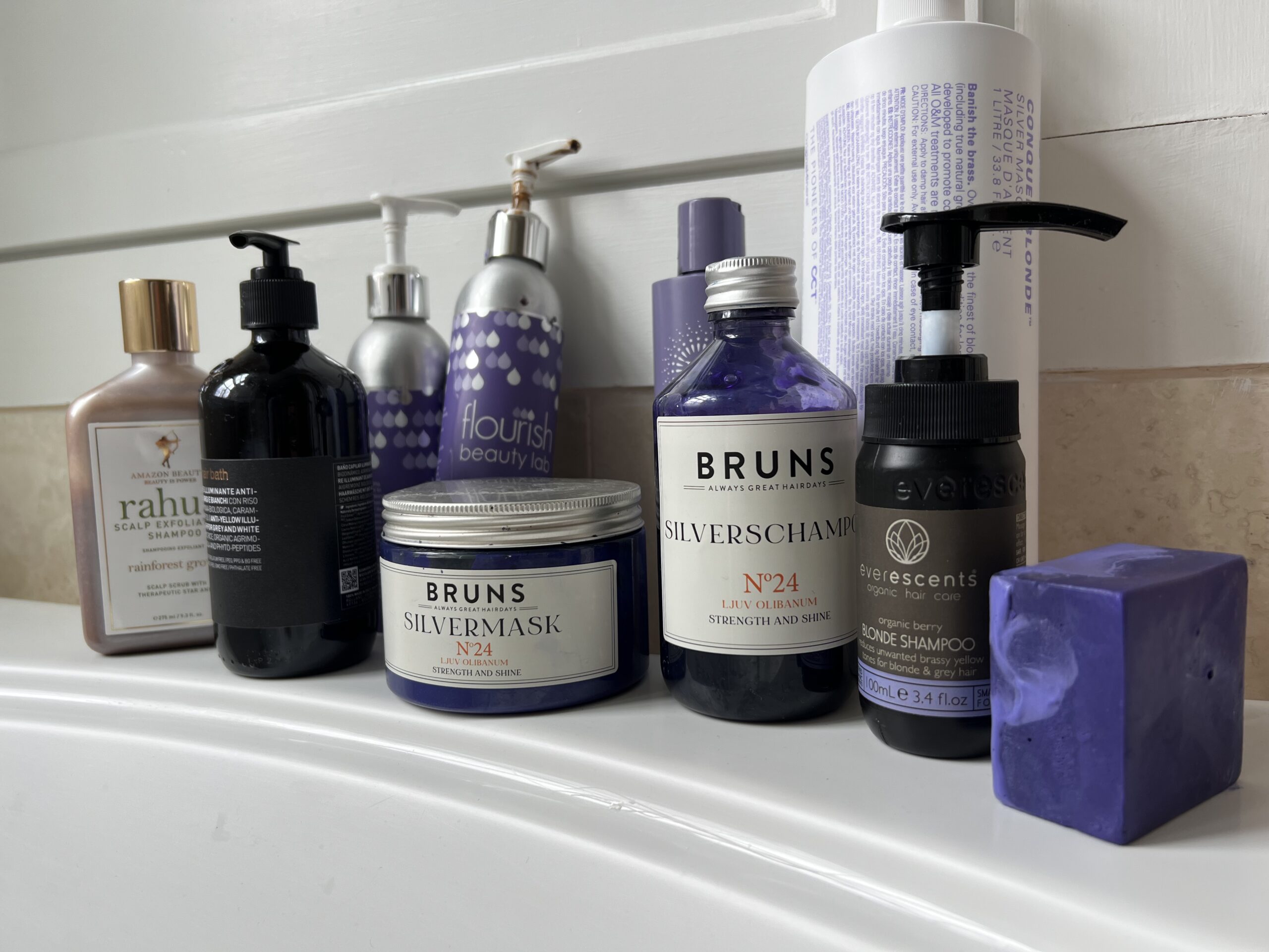 A collection of purple shampoos lined up on a bathroom sink.