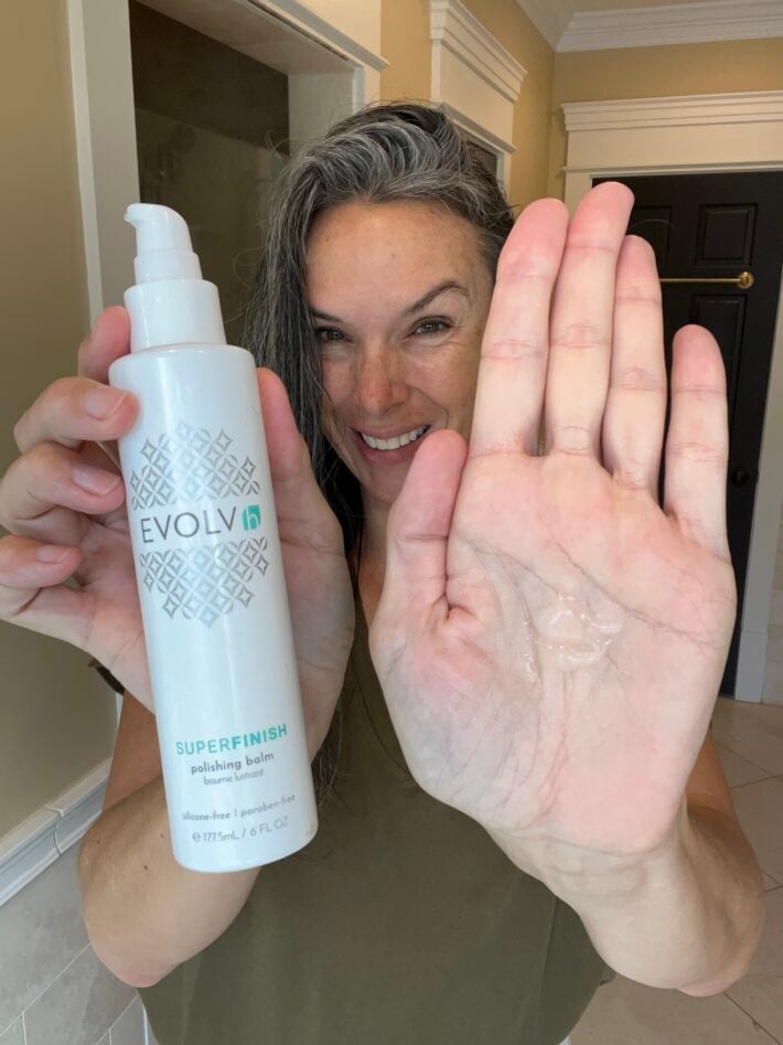 A woman holding up a bottle of EVOLVh's Superfinish polishing balm.