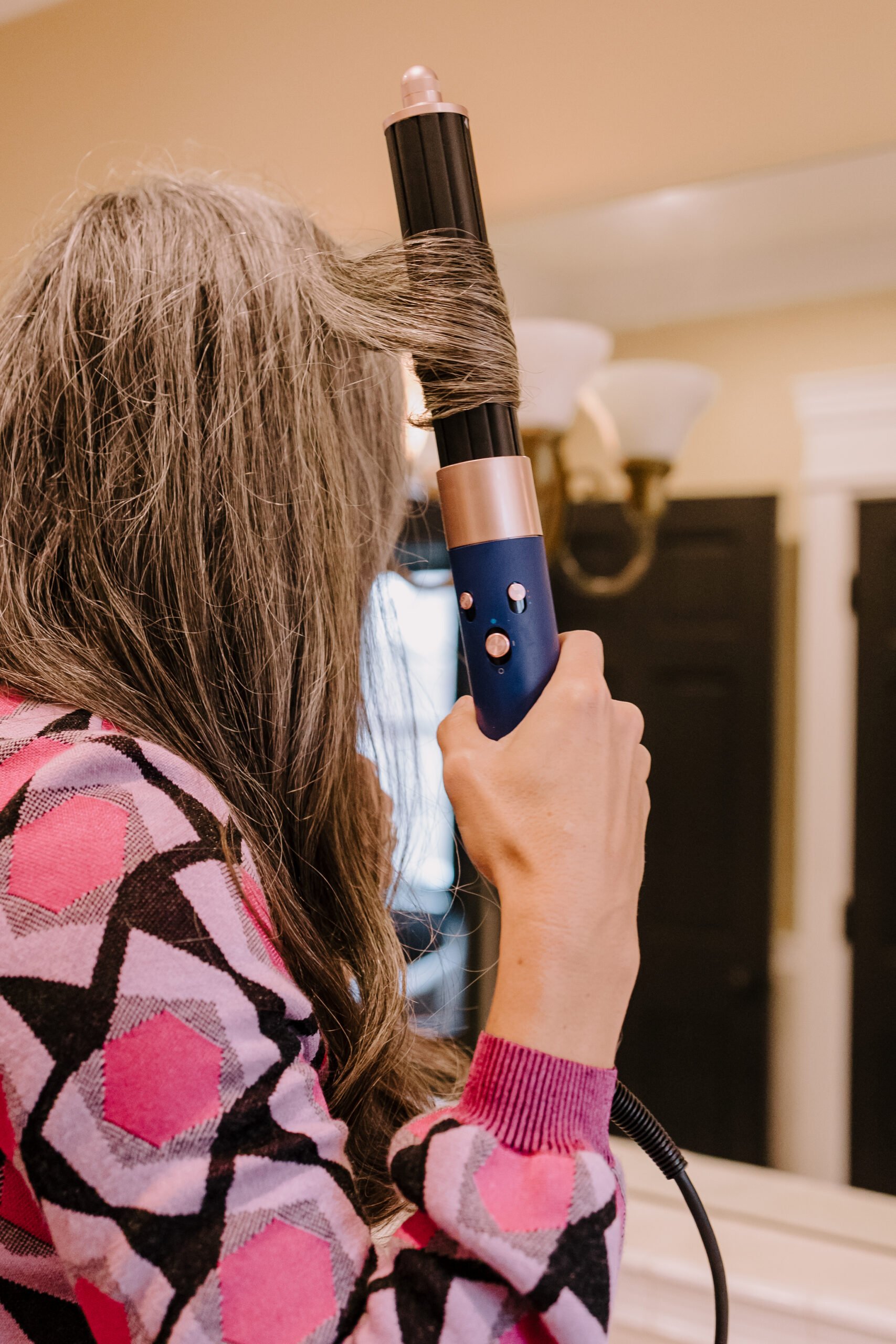 a woman with long gray hair curls her hair with the dyson airwrap.
