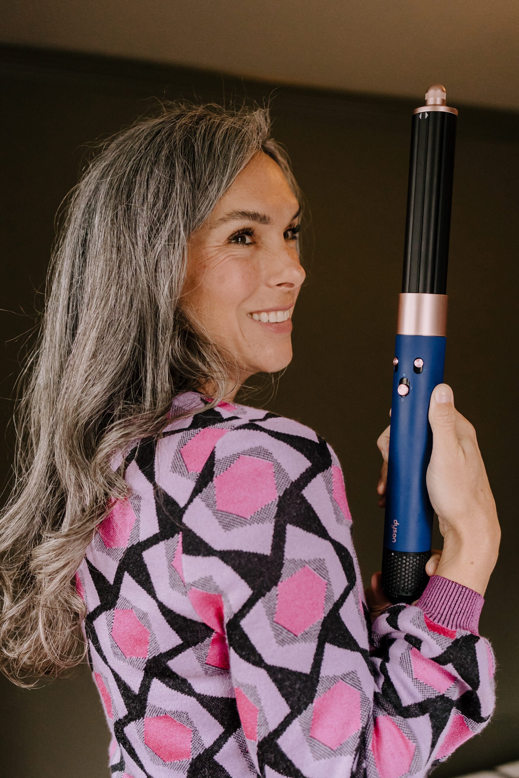 A woman with long gray hair holds up the Dyson Airwrap